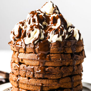 a stack of chocolate chaffles with whipped cream and drizzled with chocolate sauce