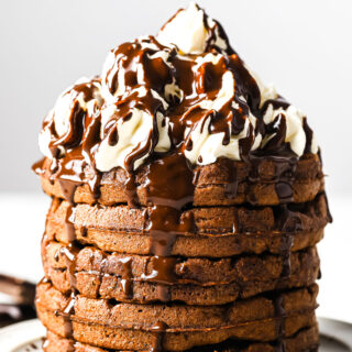 a stack of chocolate chaffles with whipped cream and drizzled with chocolate sauce