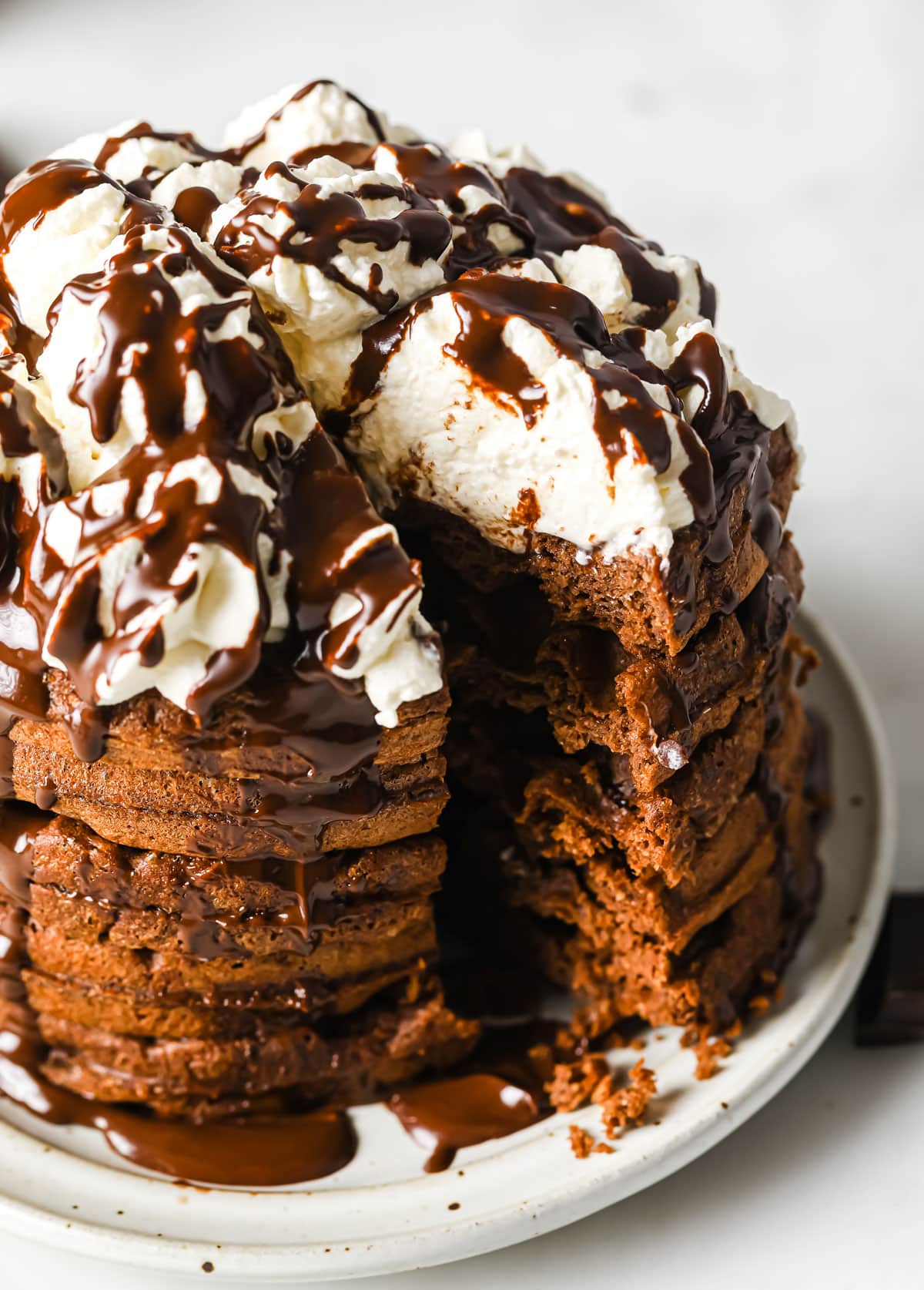 a stack of chocolate Chaffles sliced like a cake, showing the inside, and topped with whipped cream and chocolate sauce