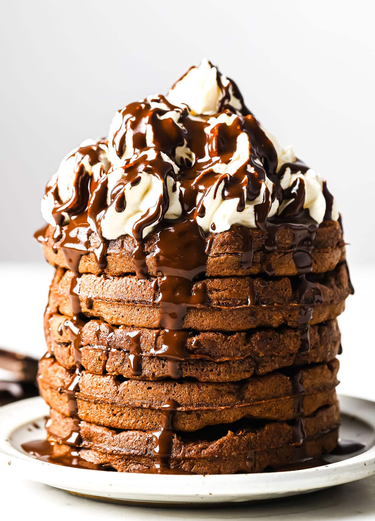 a stack of chocolate Chaffles topped with whipping cream and chocolate sauce