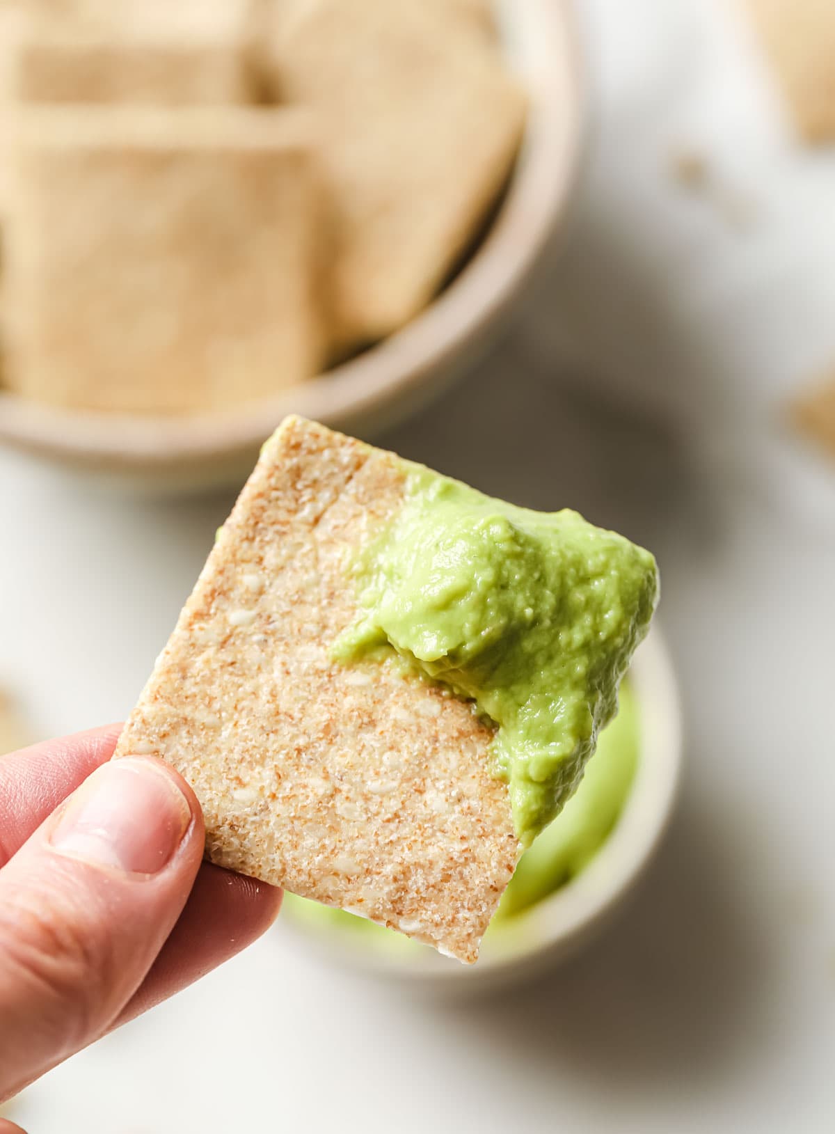 hand holding a chia cracker dipped in guacamole