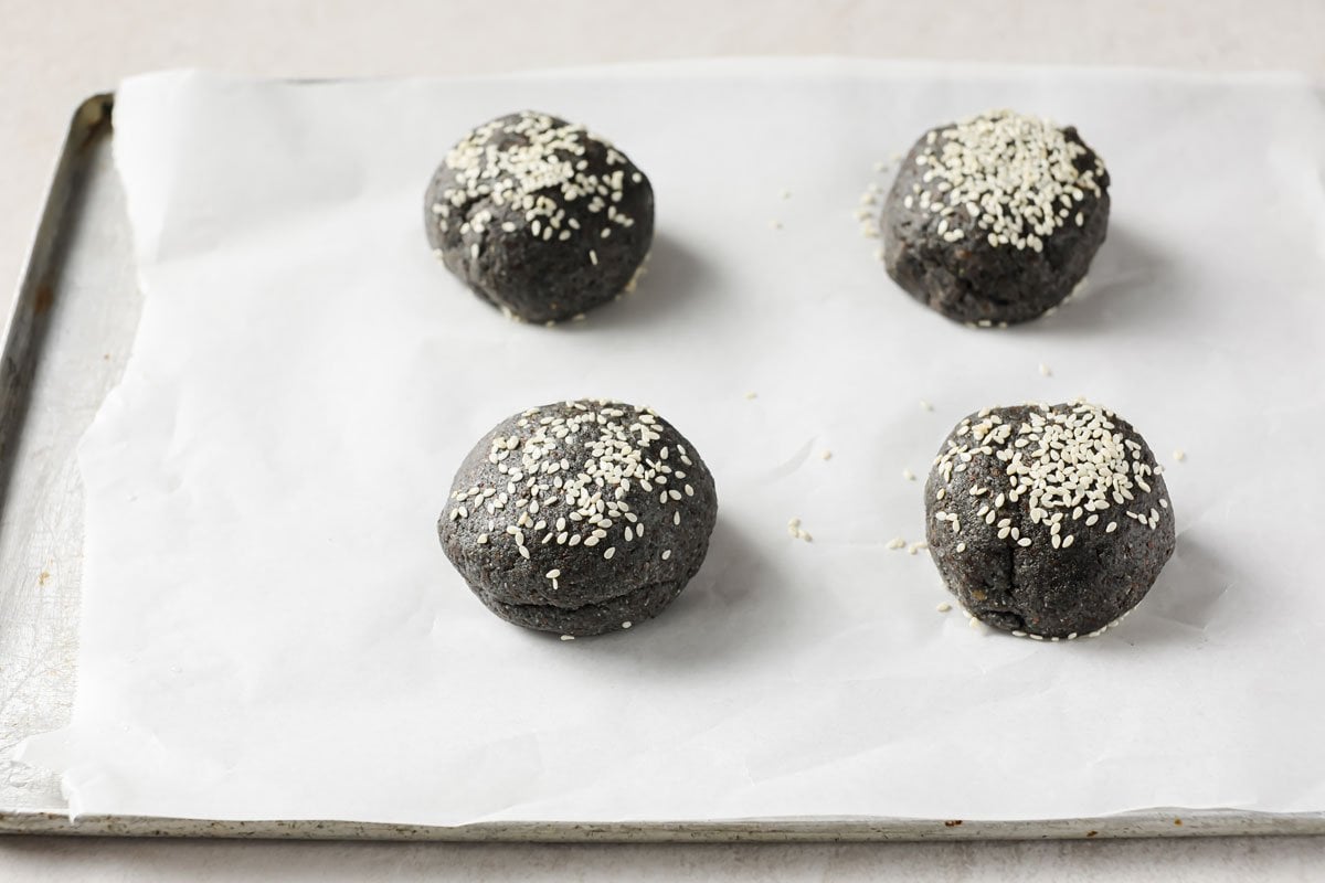 black burger buns on a baking sheet before baking