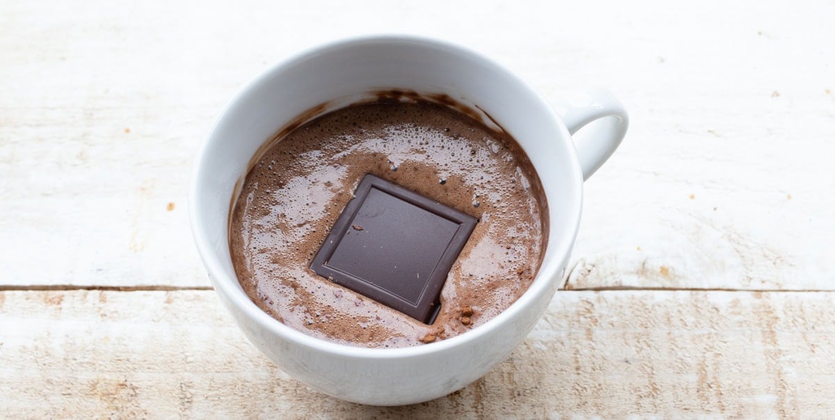 chocolate batter in a mug with a square of dark chocolate in the centre