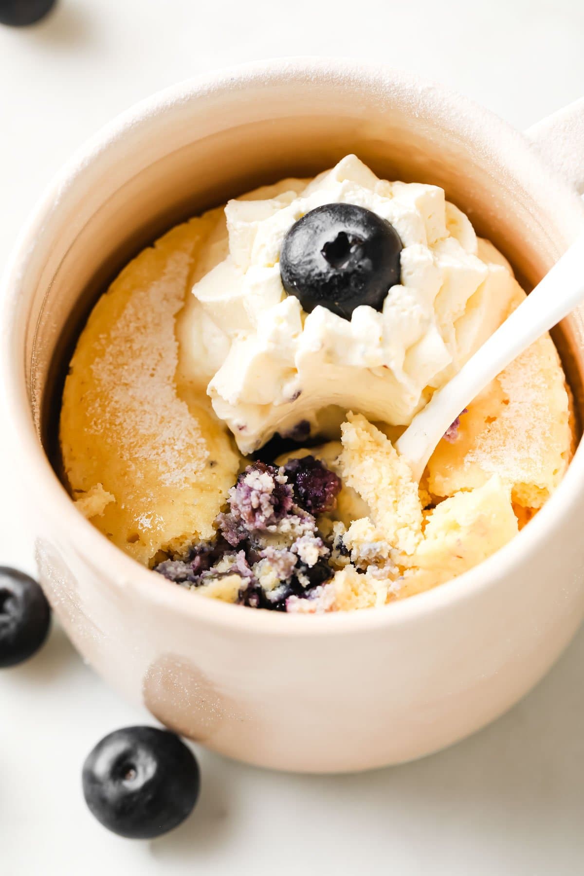 a cake in a mug topped with whipped cream and blueberries
