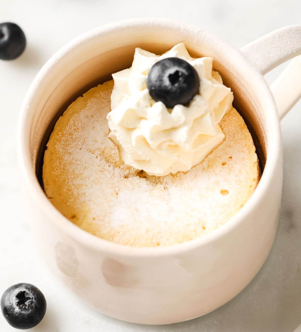a mug cake with a dollop of whipped cream and a blueberry