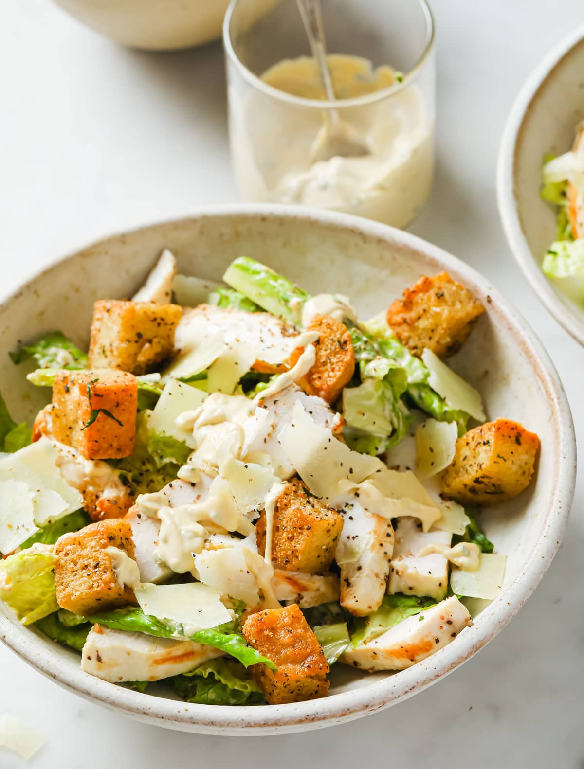 a plate with chicken Caesar salad and a glass with dressing