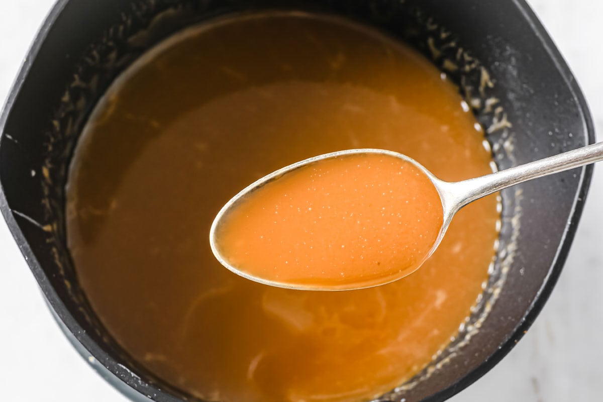 Spoon filled with caramel over a saucepan with caramel.
