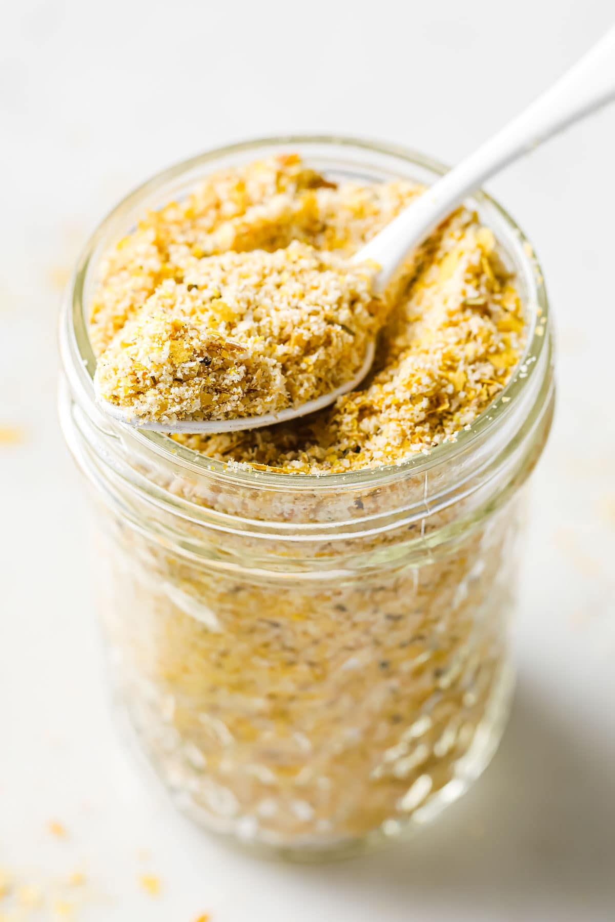 a spoon filled with breadcrumbs on top of a glass jar