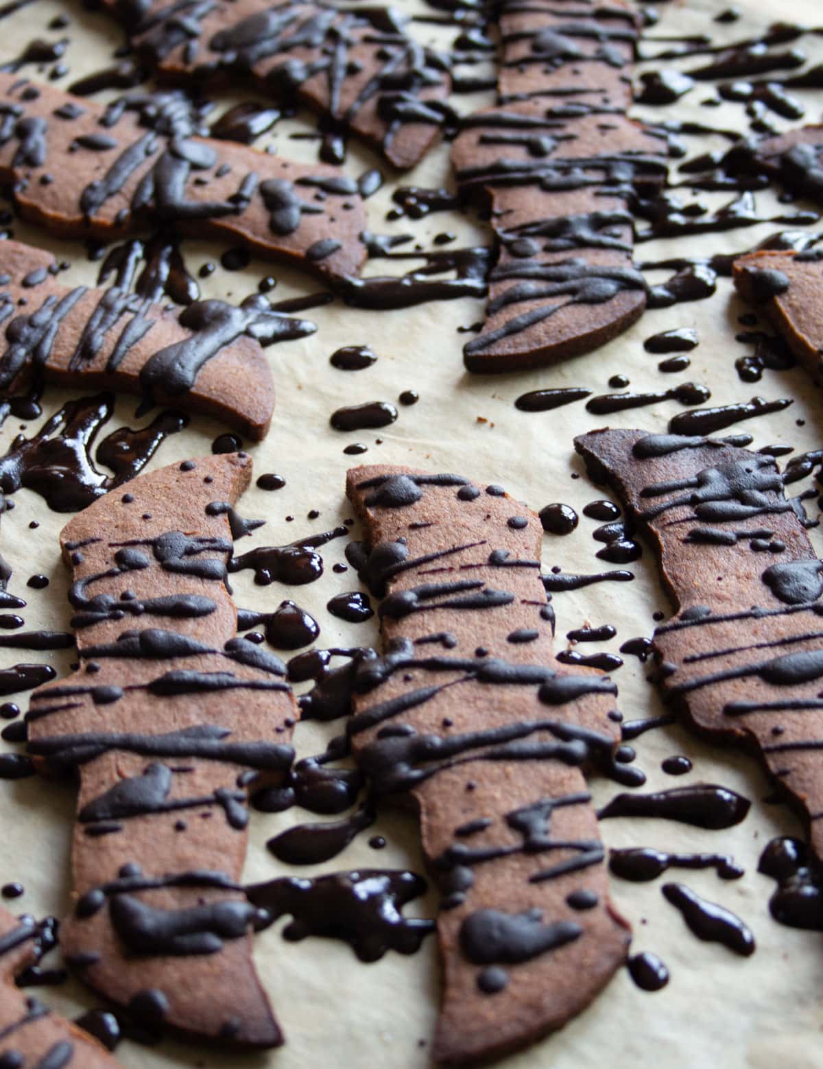 Baked chocolate cookies on parchment paper drizzled with dark chocolate.