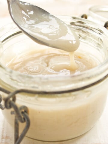 A glass jar with condensed milk and a spoon.