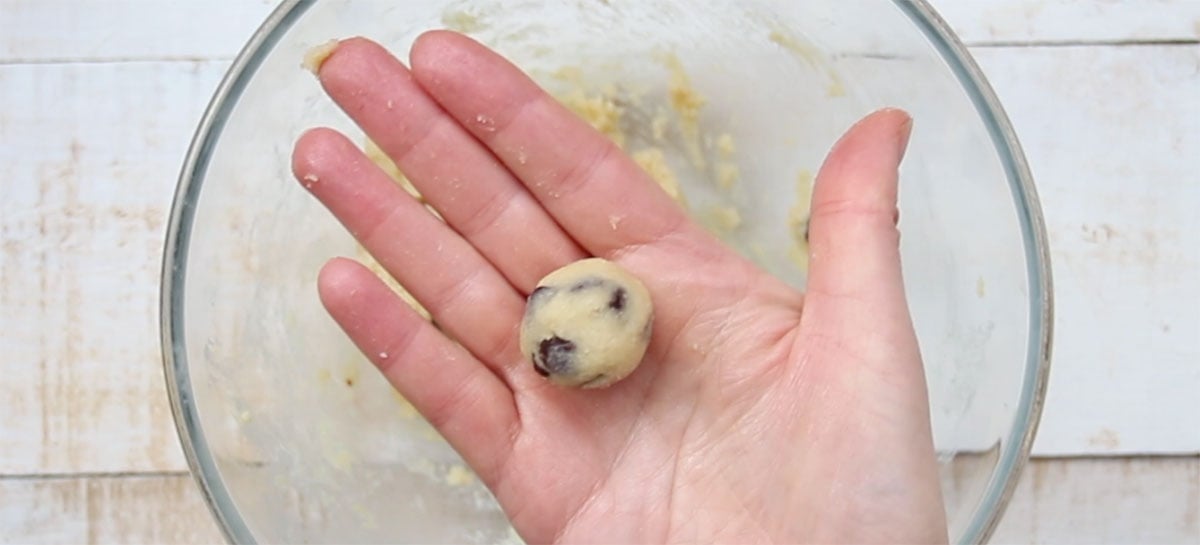 Hand holding a freshly rolled cookie dough ball.