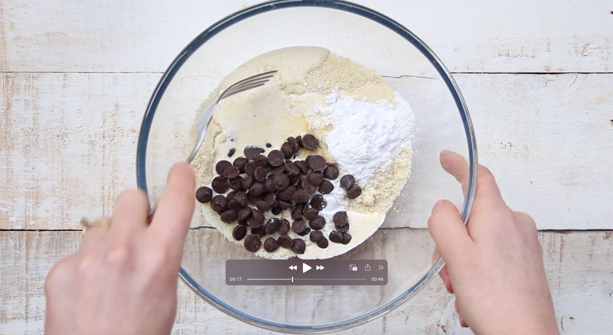 Ingredients for cookie dough in a bowl - almond flour, cream, sweetener and chocolate chips, about to be mixed with a fork.