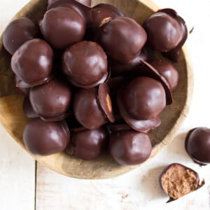 A wooden bowl with chocolate coated almond butter truffles.