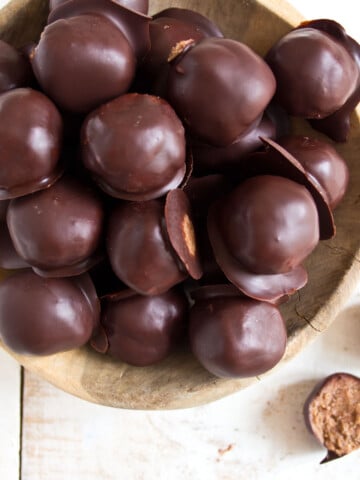 A wooden bowl with chocolate coated almond butter truffles.