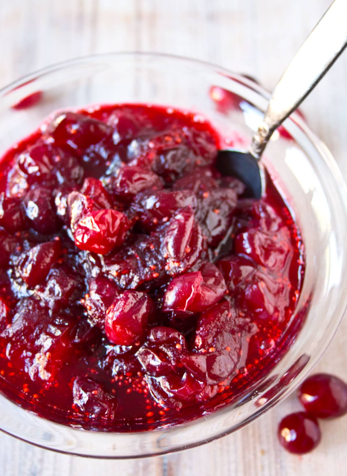 A glass bowl with cranberry sauce and a spoon.