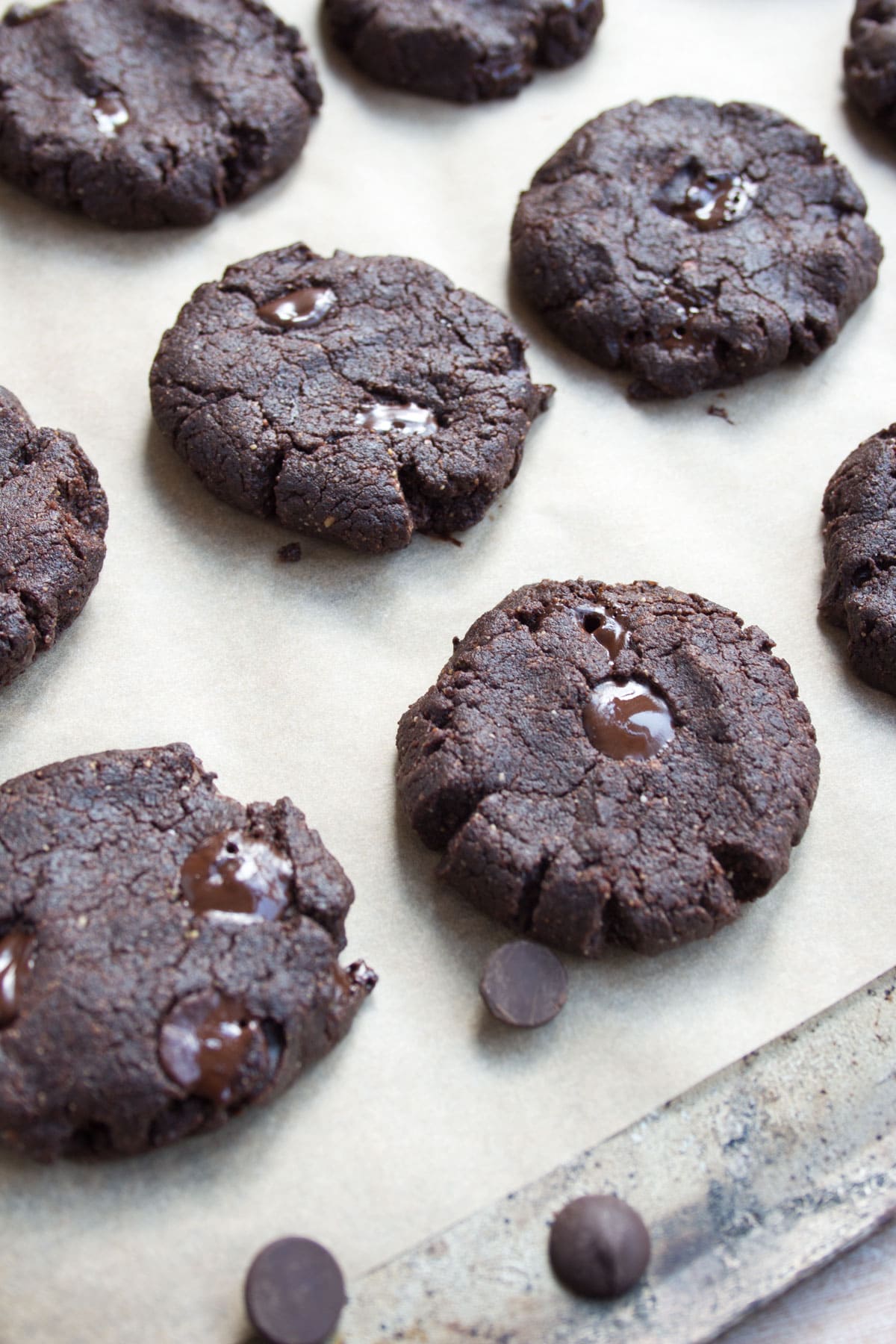Baked brownie cookies with melted chocolate chips on a cookie sheet lined with parchment paper.