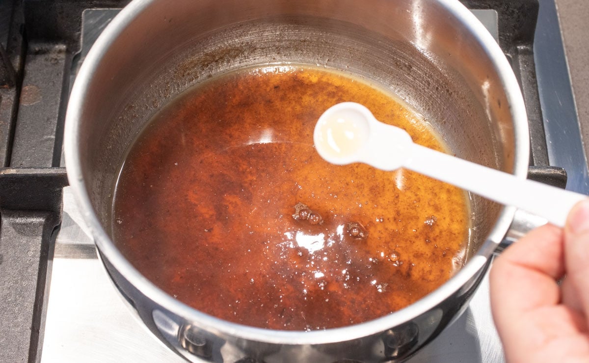 Adding a spoonful of brandy to the caramel in a pot.
