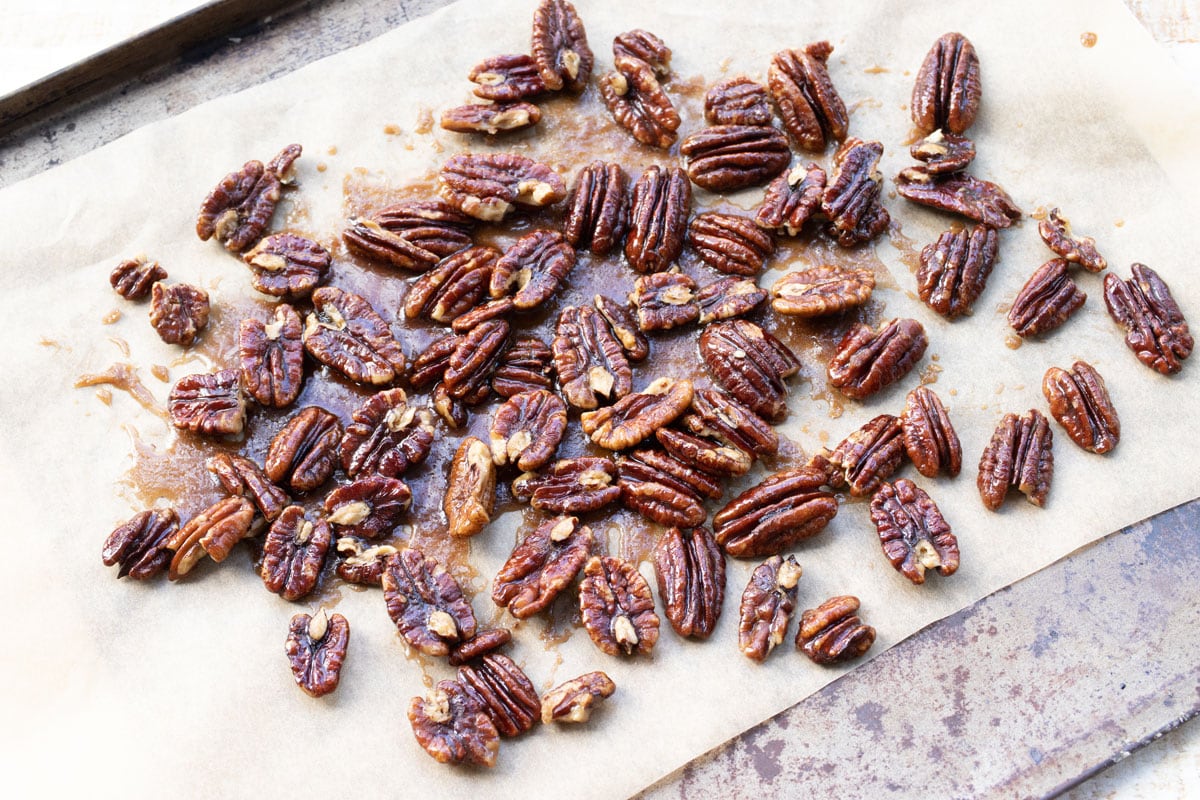 Candied pecans drying on a cookie sheet lined with parchment paper.
