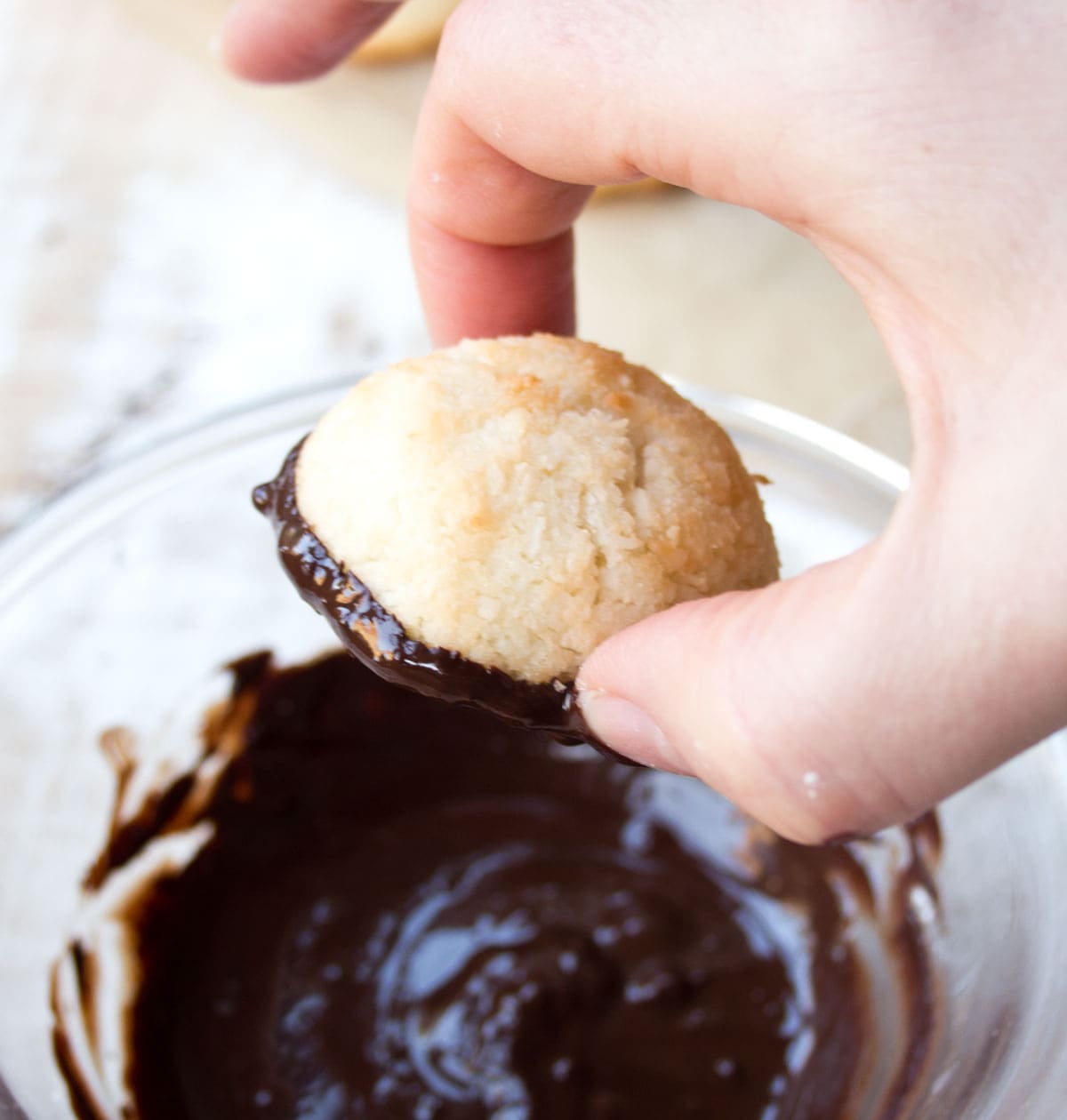 Dipping a macaroon into a bowl with melted chocolate.