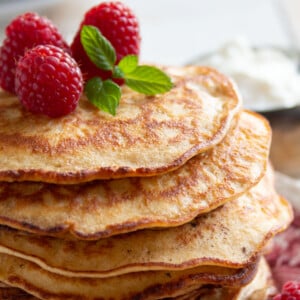 A stack of almond cream cheese pancakes topped with raspberries.