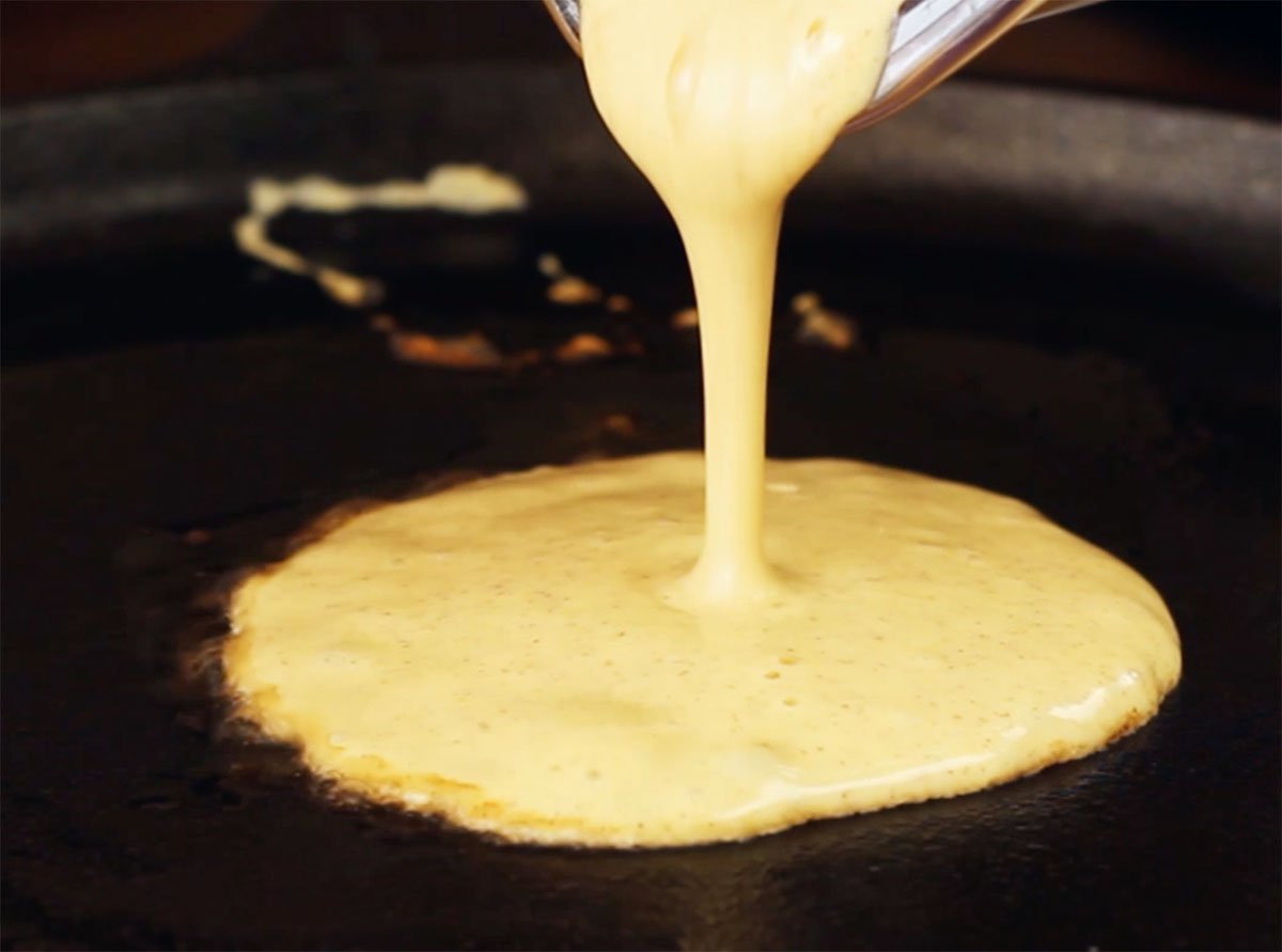 Pouring pancake batter into a frying pan.