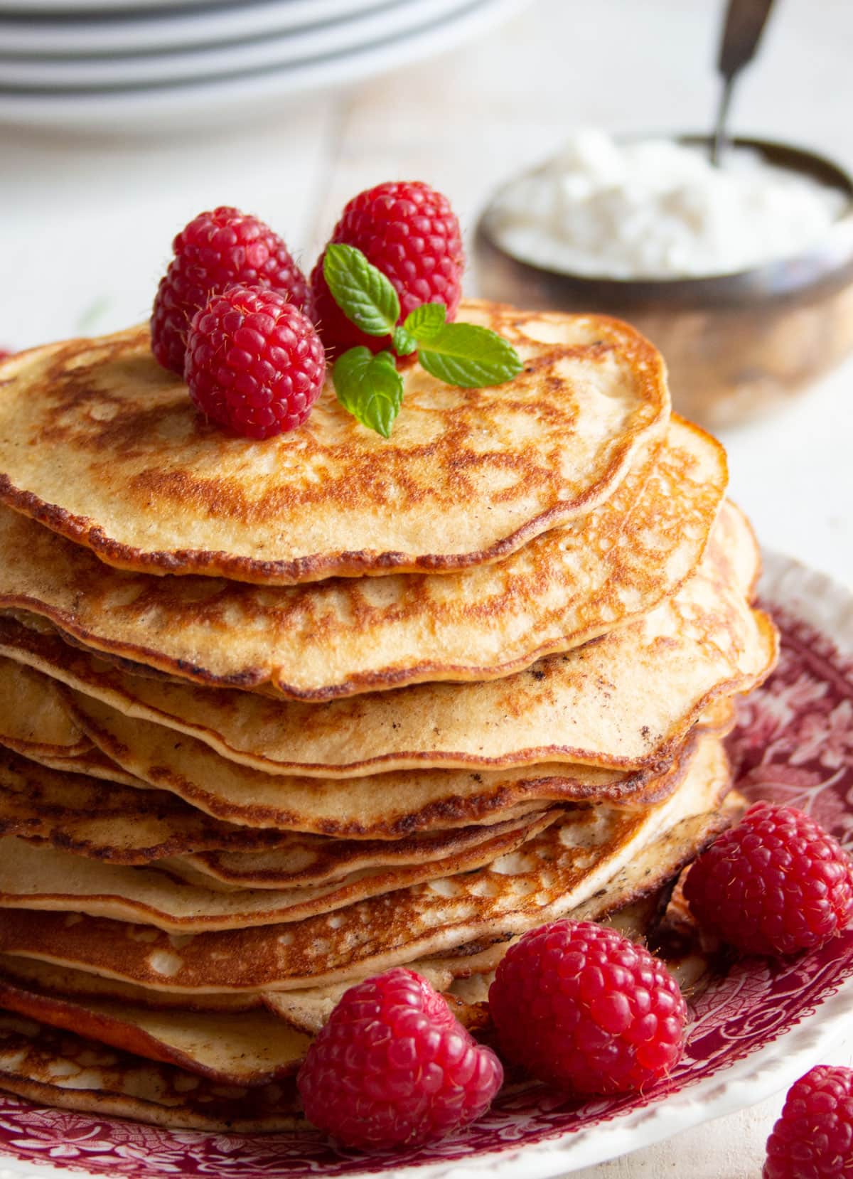 A stack of pancakes topped with raspberries and a bowl with yoghurt.
