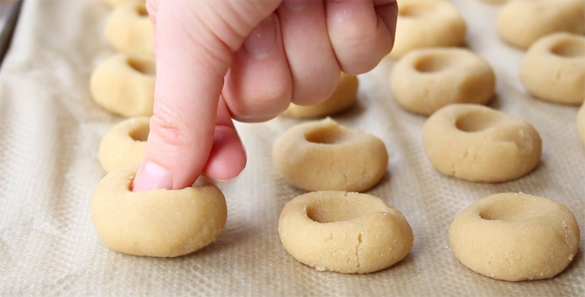 Pressing a thumb into cookie dough to make indentations.