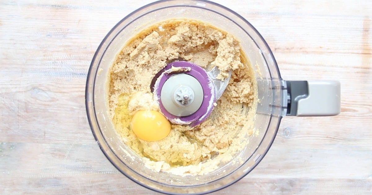 Cookie dough and an egg in a food processor bowl.