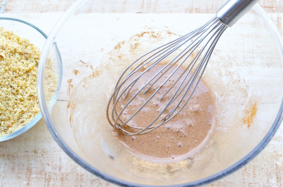 Beaten egg with cinnamon and sweetener in a bowl with a balloon whisk.