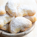 Crescent shaped cookies in a bowl dusted with powdered sweeter.