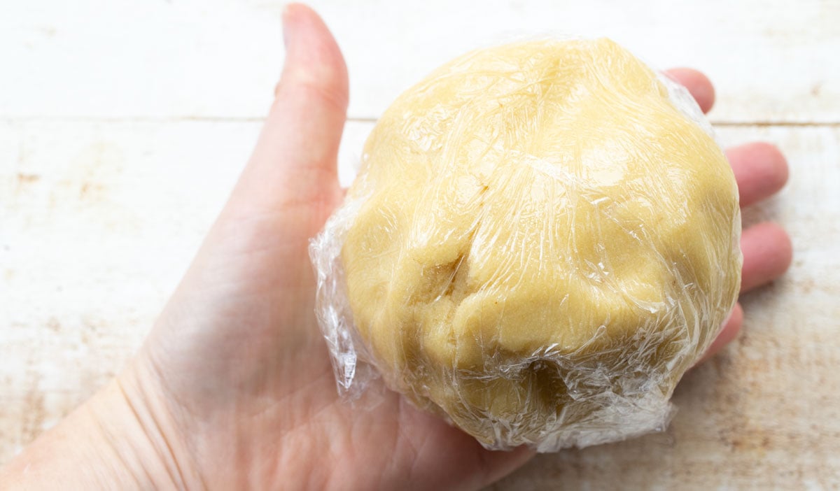 A cookie dough ball wrapped in cling film, held by a hand.