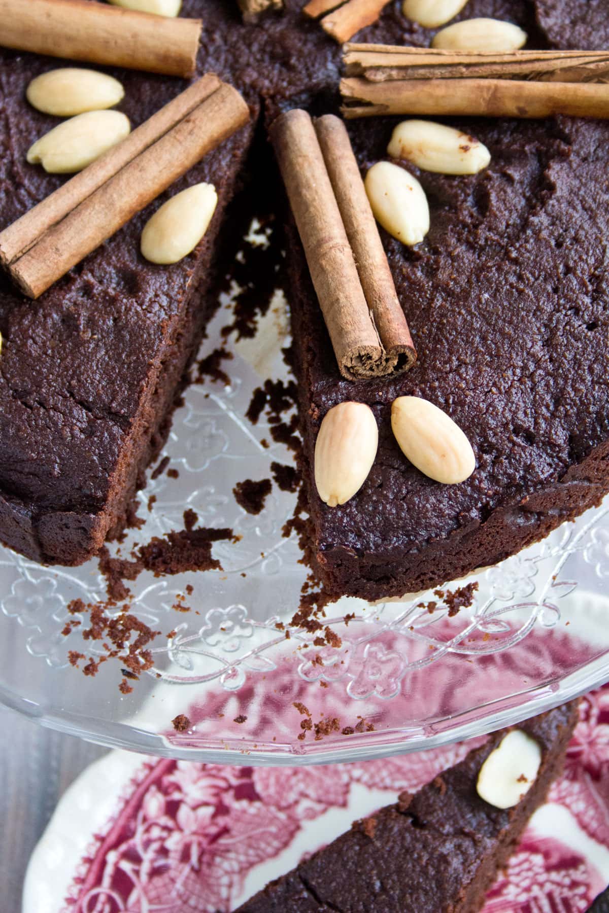 A chocolate cake decorated with cinnamon sticks and almonds on a cake stand.
