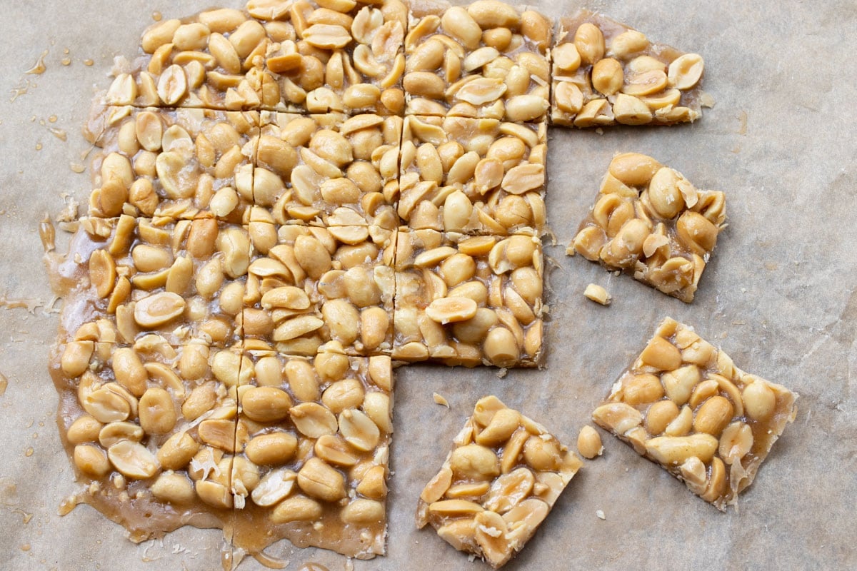 Peanut brittle on parchment paper sliced into squares.