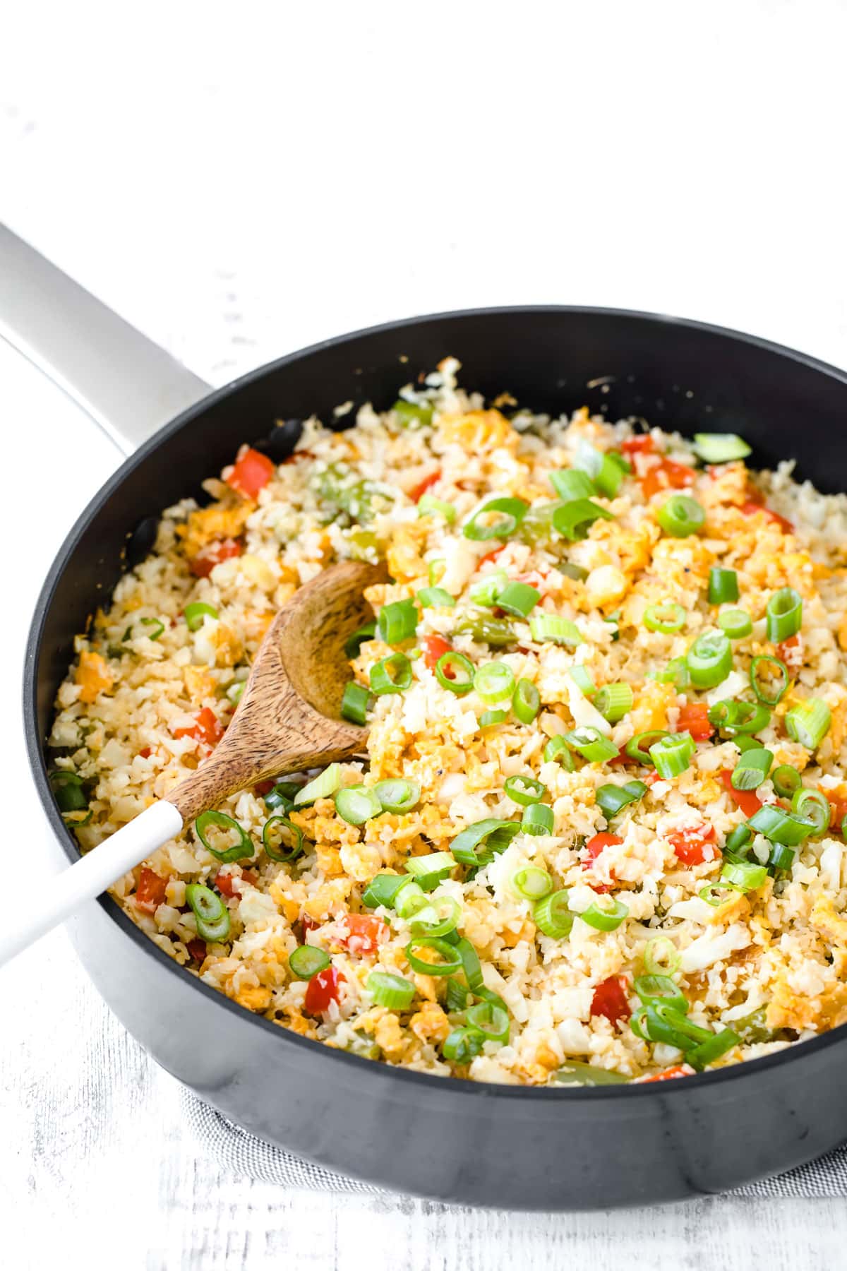 A black skillet with cauliflower fried rice, topped with chopped green onions.