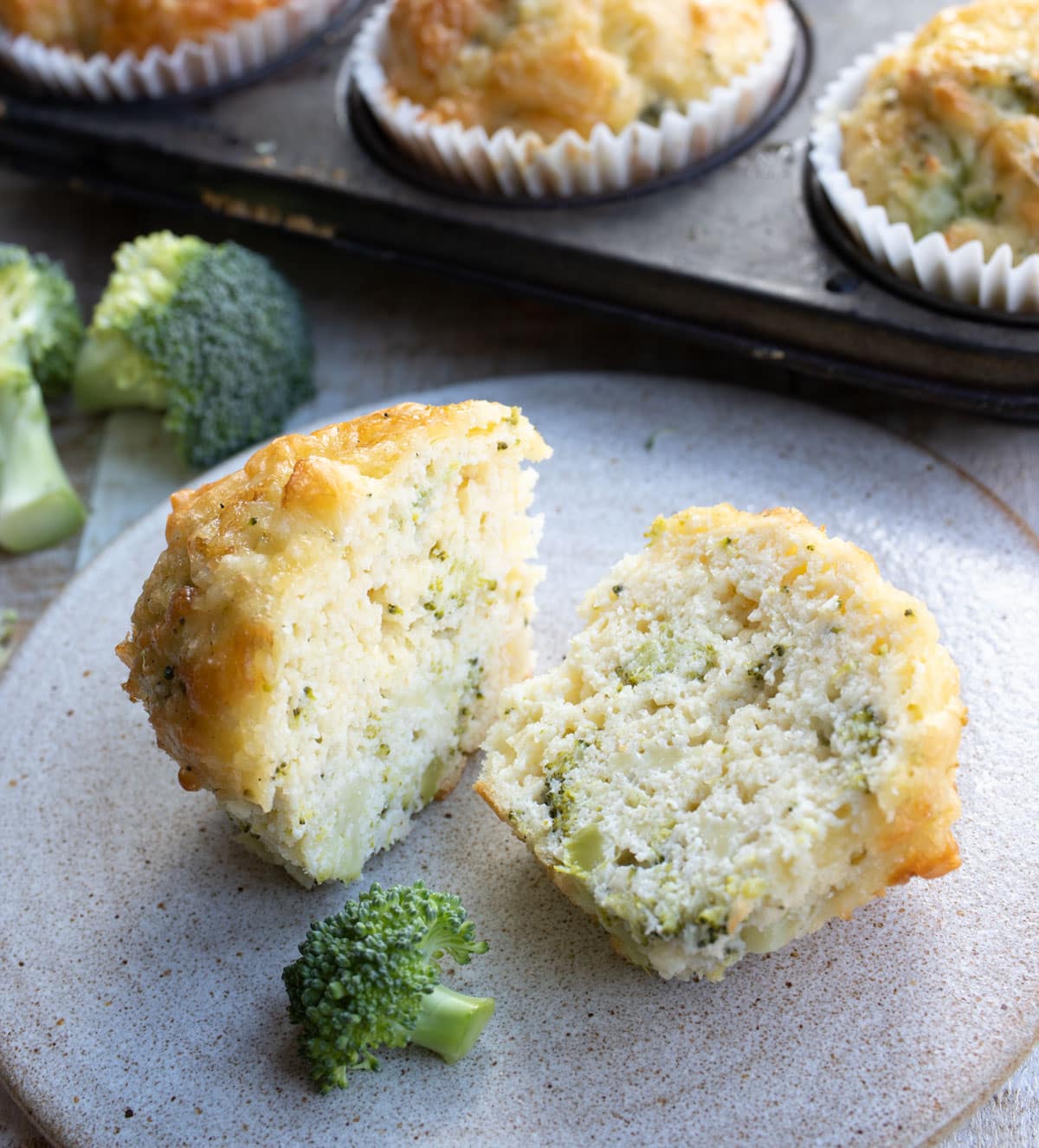 A savoury muffin with broccoli on a plate, sliced in half.