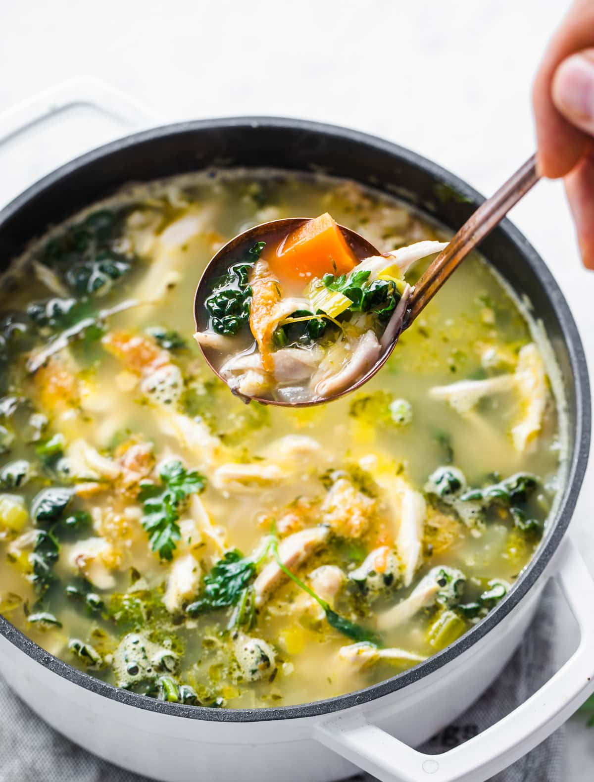 A pot with chicken soup and a ladle with soup.