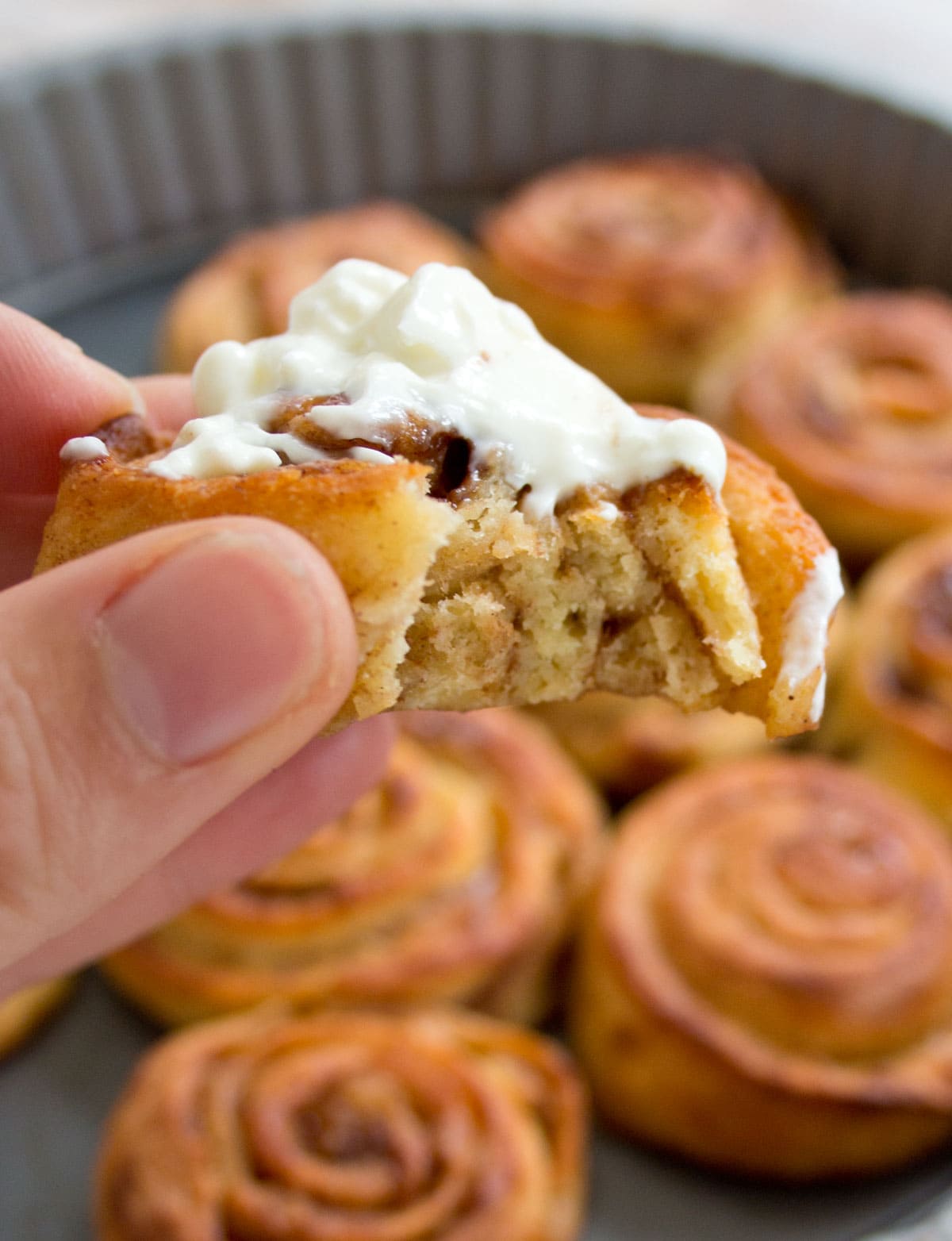 Hand holding a bitten cinnamon roll with frosting.