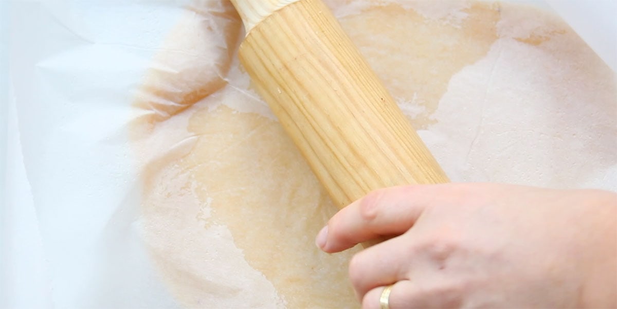 Rolling out dough between 2 sheets pf parchment paper using a rolling pin.