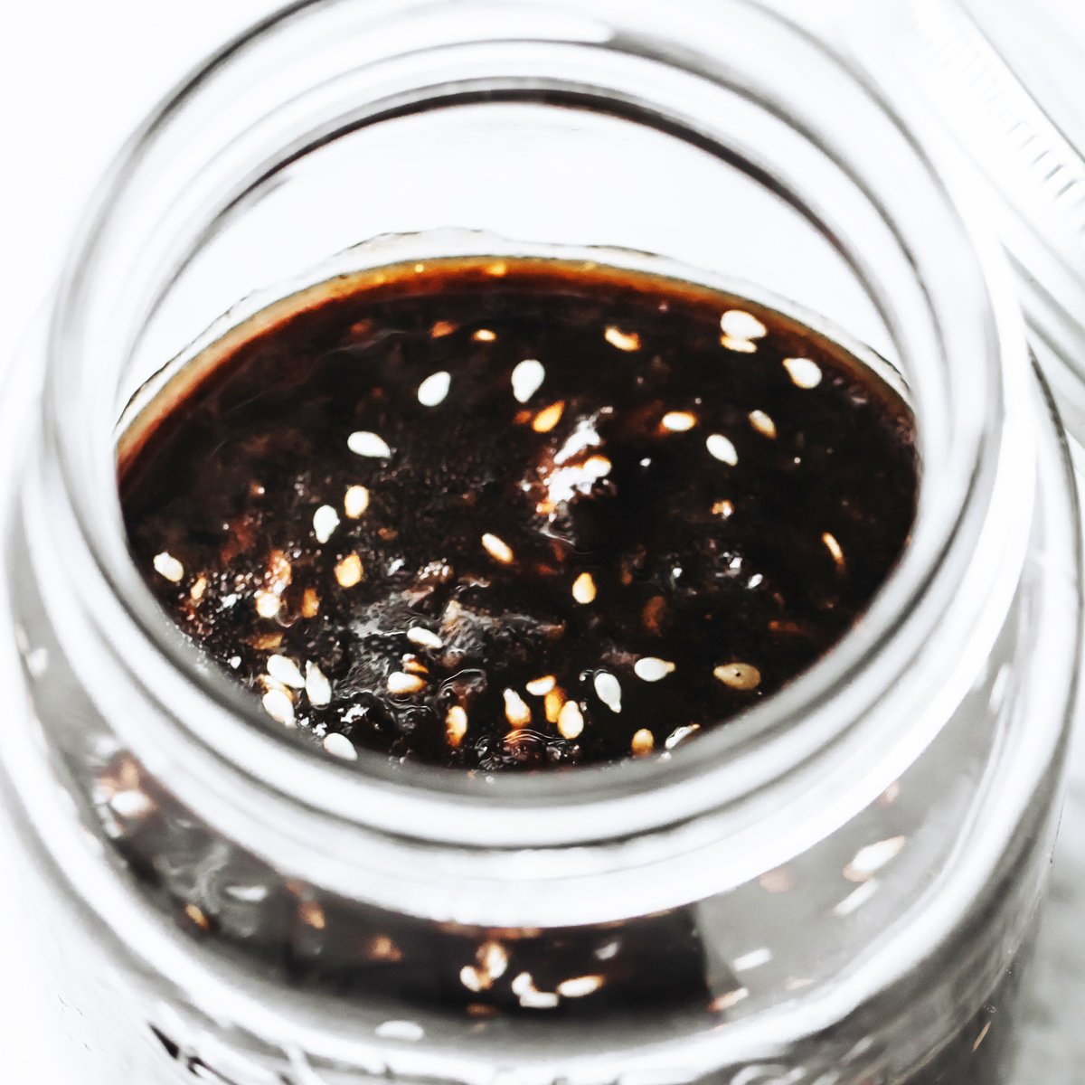 Teriyaki sauce with sesame seeds in a glass jar.
