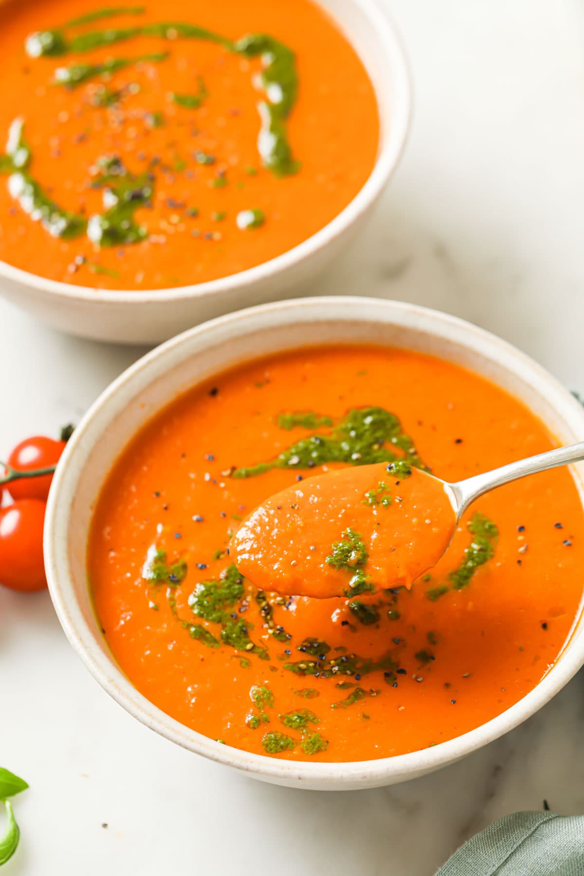 Two bowls filled with tomato soup and a spoon full of soup.