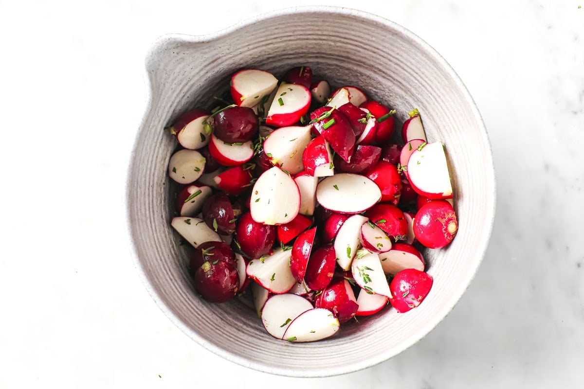 Prepared radishes tossed in oil and herbs in a bowl.