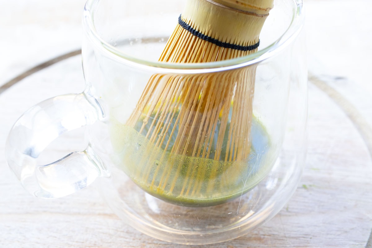 Mixing matcha powder and water with a bamboo whisk.