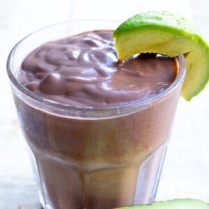 A chocolate avocado smoothie with a slice of avocado om the rim