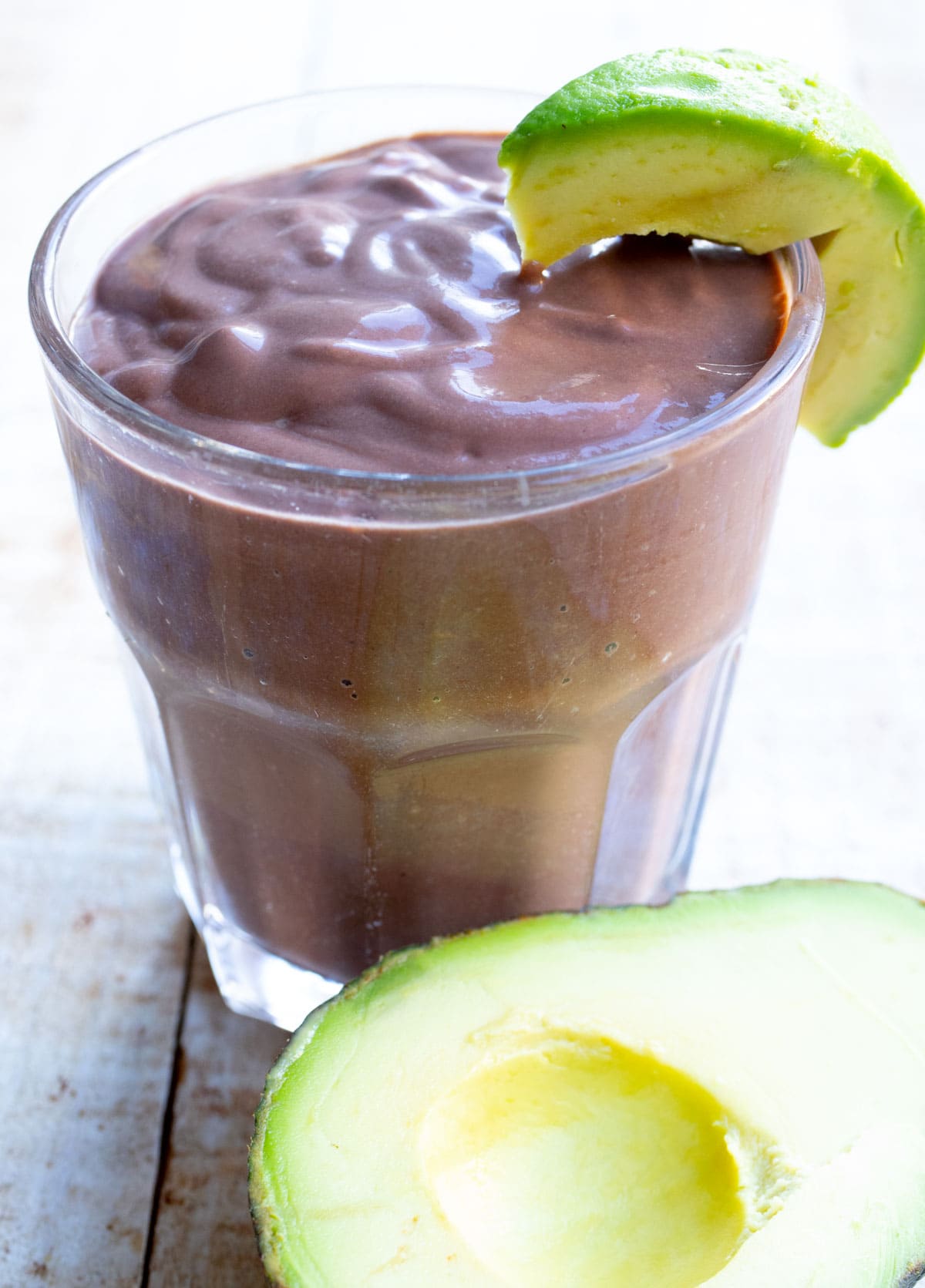 Chocolate avocado smoothie in a glass with a slice of avocado on the rim.