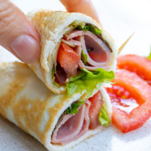 An egg white wrap sliced in half and filled with ham and greens.