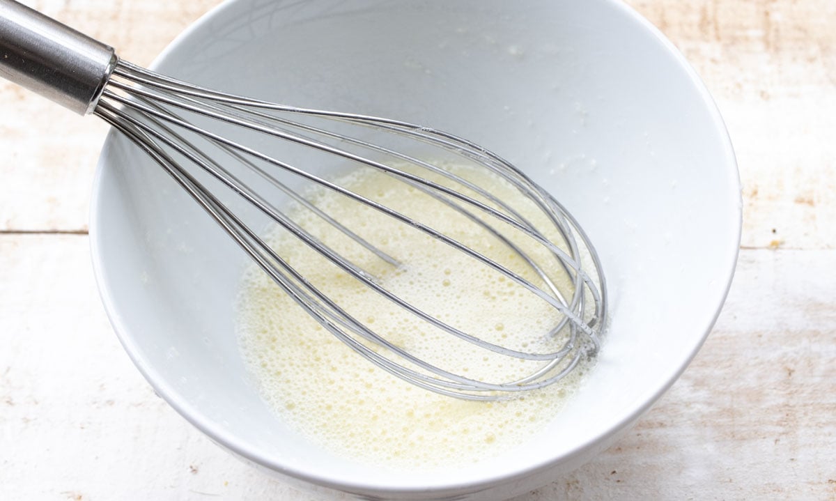 Blended egg whites in a bowl and a balloon whisk.