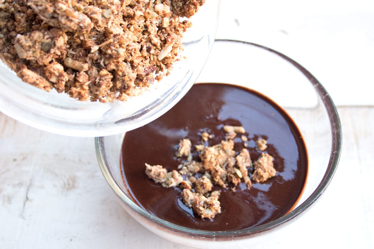 Adding keto granola to a bowl with melted chocolate.