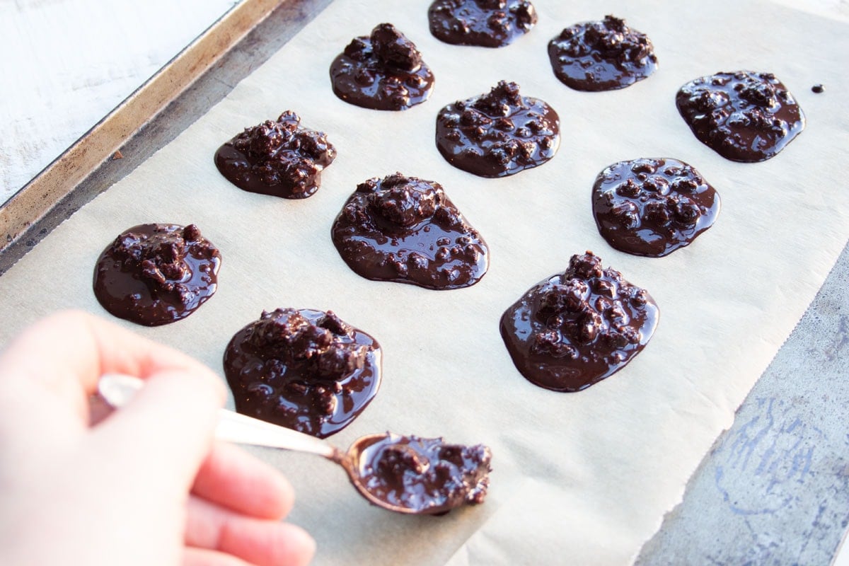 Dropping melted chocolate onto parchment paper to create pralines.