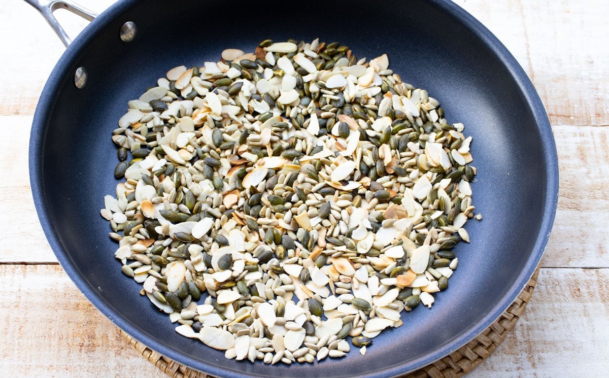 Toasting seeds and sliced almonds in a frying pan.