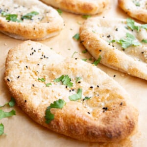 A naan bread topped with black and white sesame seeds and chopped coriander.